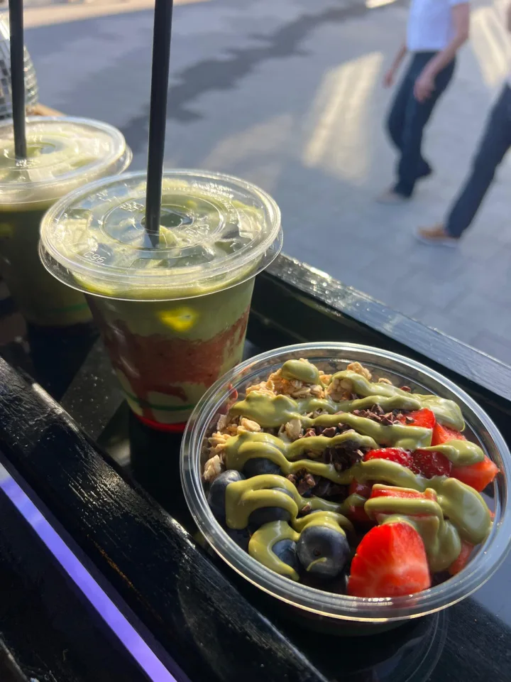 A fruit bowl with a green drizzle alongside iced matcha drinks