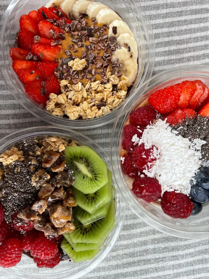 Three different bowls with fresh fruit, granola, coconut and peanut butter